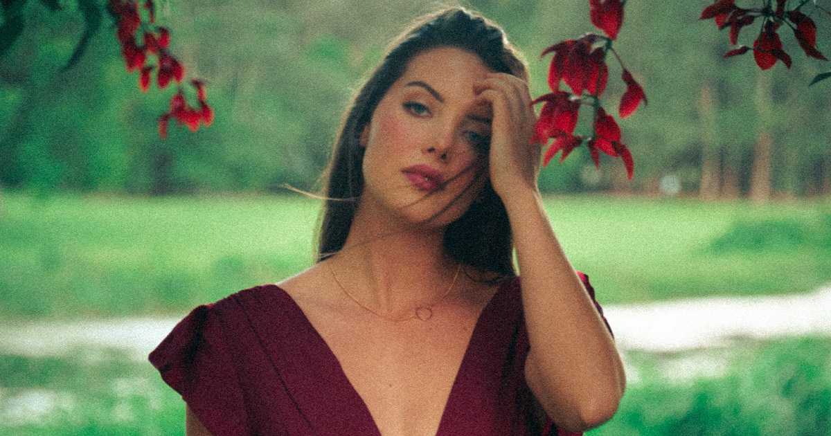 Woman in a deep red dress posing outdoors beneath red leaves, captured in soft natural light - fashion portrait by Gold Coast photographer Bora Veli.