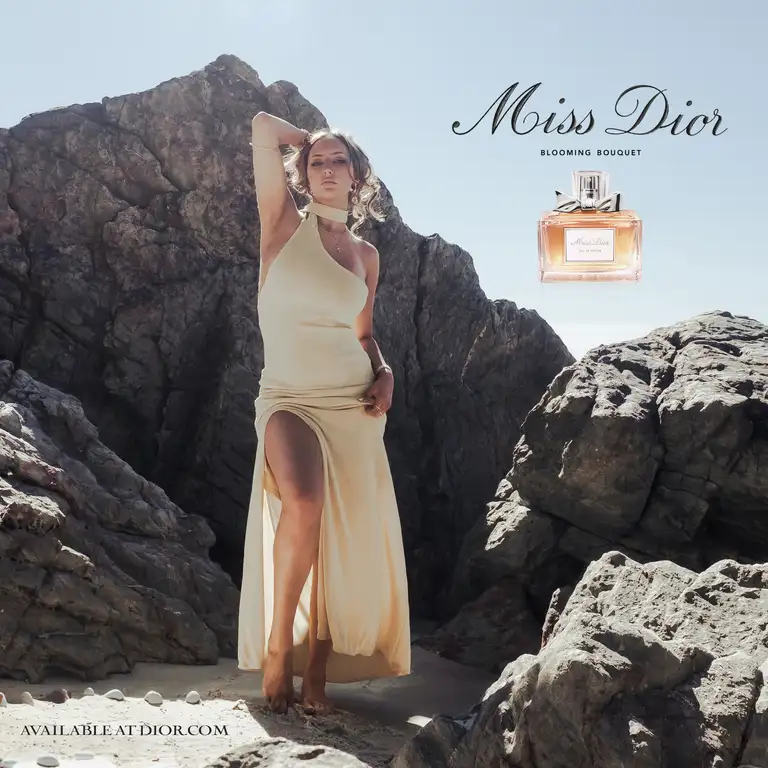 Commercial fashion photograph of a model wearing a cream dress posed against dramatic coastal rocks on the Gold Coast, captured in warm natural light with a refined beach editorial style.
