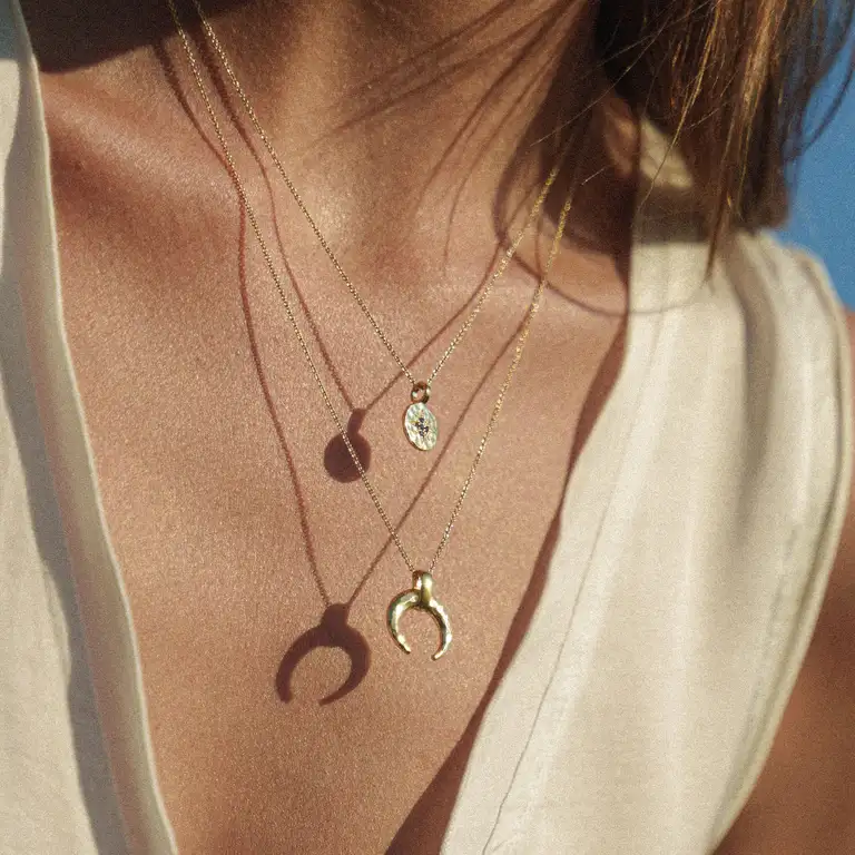 Detailed shot of layered gold necklaces from a jewellery brand resting on the model’s chest, captured in warm golden hour light with a soft, film-style finish.