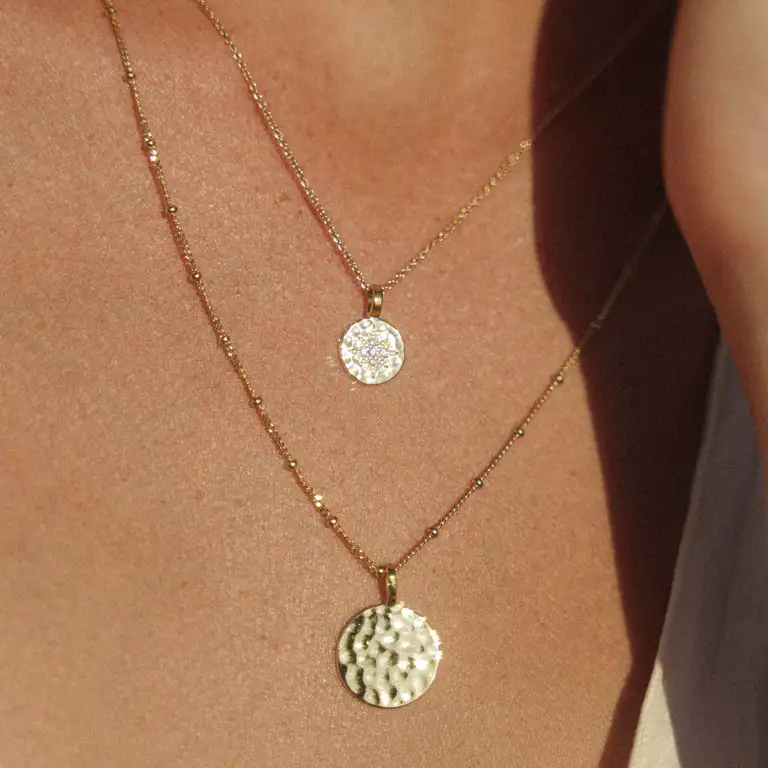 Close-up of textured circular gold pendant necklaces from a jewellery brand, photographed in warm natural light for a soft, cinematic film look.