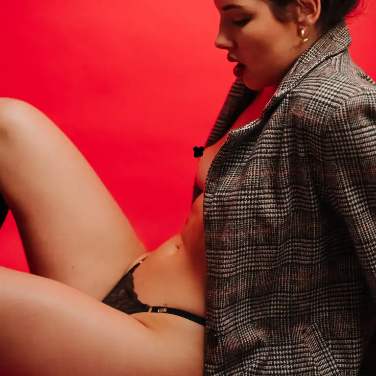 Editorial lingerie image of a model wearing black lace underwear and an oversized blazer in Australia, posed against a bold red backdrop with a confident, fashion-forward style.